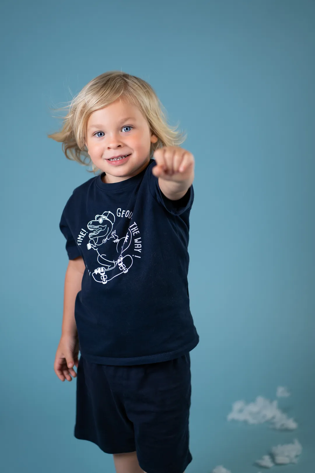 Porträt eines Jungen, er zeigt mit der Faust in die Kamera, blauer Hintergrund