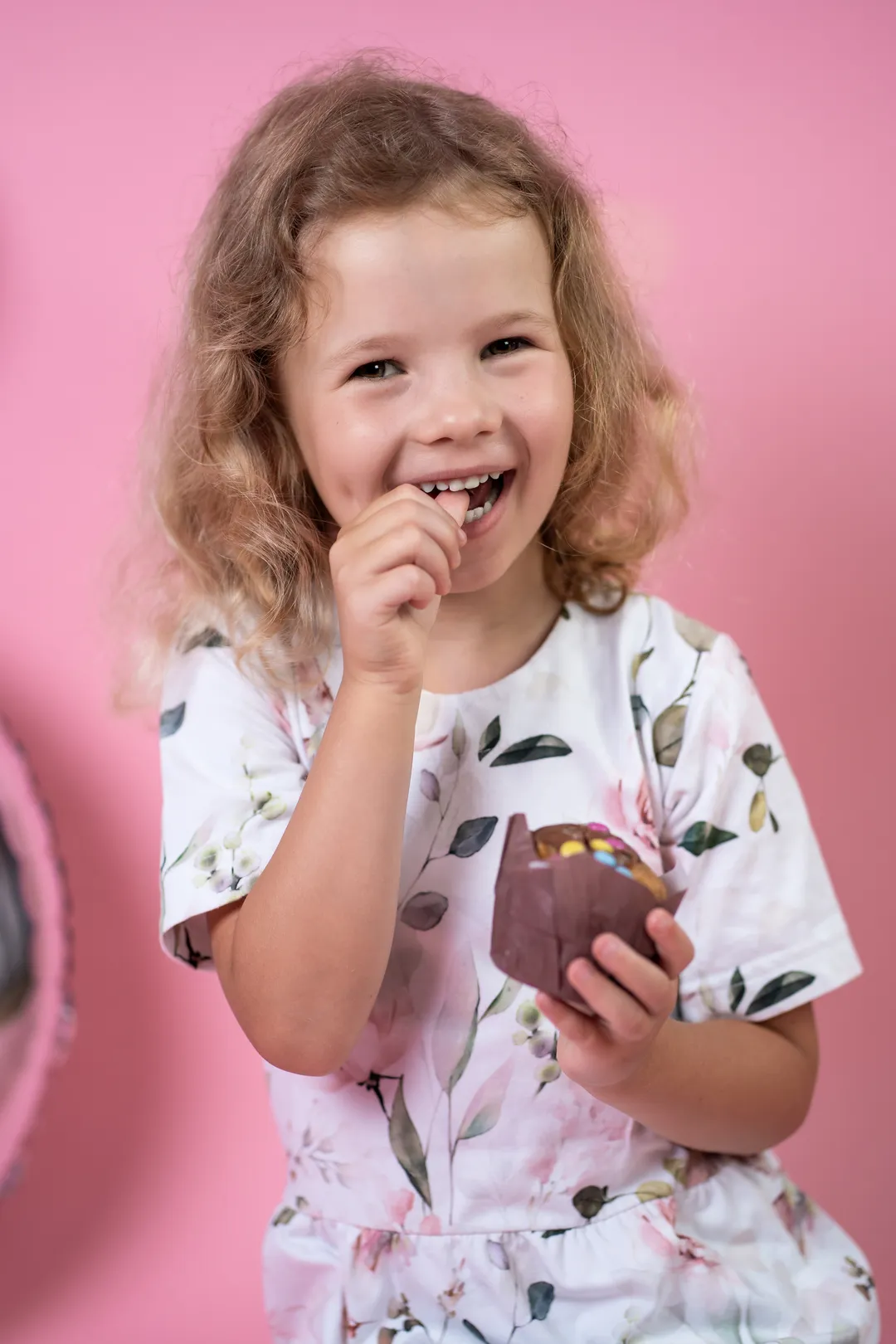 Porträt eines lächelnden Mädchens mit einem Muffin in der Hand, pinker Hintergrund